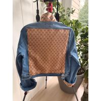 Back of medium blue denim jacket with large sand colored repeating pattern textile panel