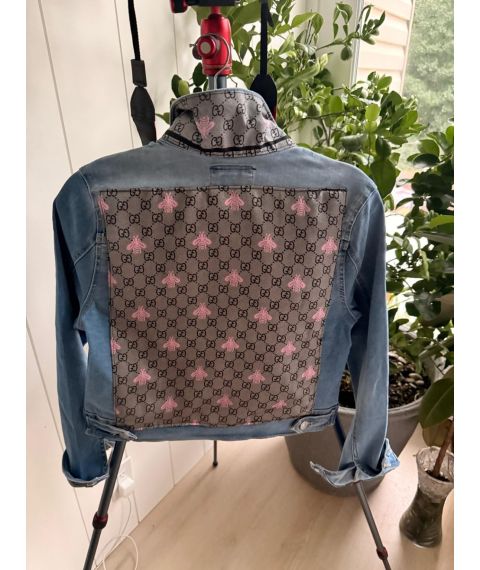 Back view of medium light-wash denim jacket with patterned panel and pink bee motifs